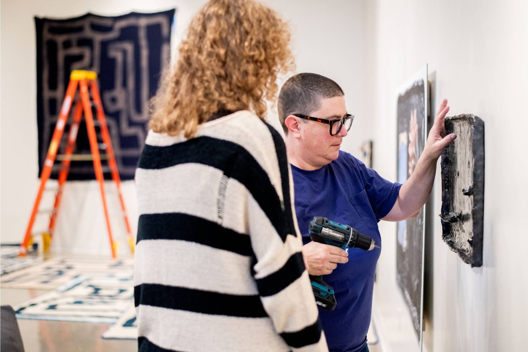 students working with Emmy Bright to hand artwork in gallery